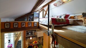 A loft-style bedroom with a bunk bed, a television, and a kitchen area with a fruit bowl and hanging lights. - C3DD Strolling (París)
