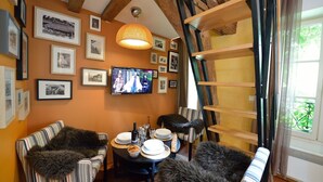 A cozy living room with a television, framed pictures, and a dining area with a table set for two. - C3DD Strolling (París)