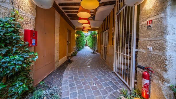 A narrow corridor with a stone-tiled floor, a fire extinguisher mounted on the wall, and a red emergency box on the left. - C3DD Strolling (París)