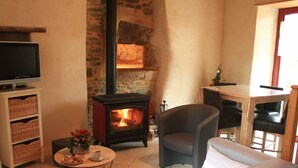 A cozy living room with a stone fireplace, a television, wicker baskets, a coffee table with flowers, and a grey sofa. - Countryside house with pool and spa in Normandy (Savigny (Manche))