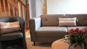 A living room with a sofa, armchair, and a coffee table with a floral arrangement. - Countryside house with pool and spa in Normandy (Savigny (Manche))