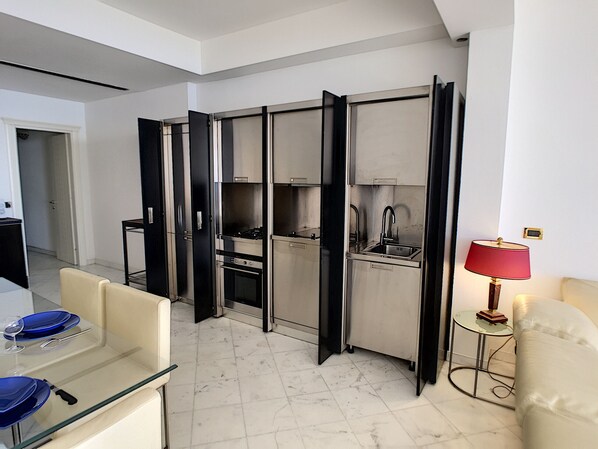 Una cocina moderna con estufa, horno y pileta integrados, y un comedor con mesa y sillas de vidrio.