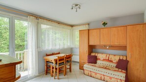 A compact room with a dining table and chairs, a sofa with patterned cushions, and wooden cabinets.