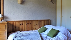 A bedroom with a wooden headboard, a bed with white bedding and green pillows, a wall-mounted basket, and a wardrobe with two doors.