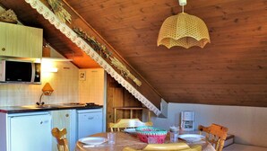 A cozy kitchen with a dining area, wooden ceiling, and a hanging light fixture.