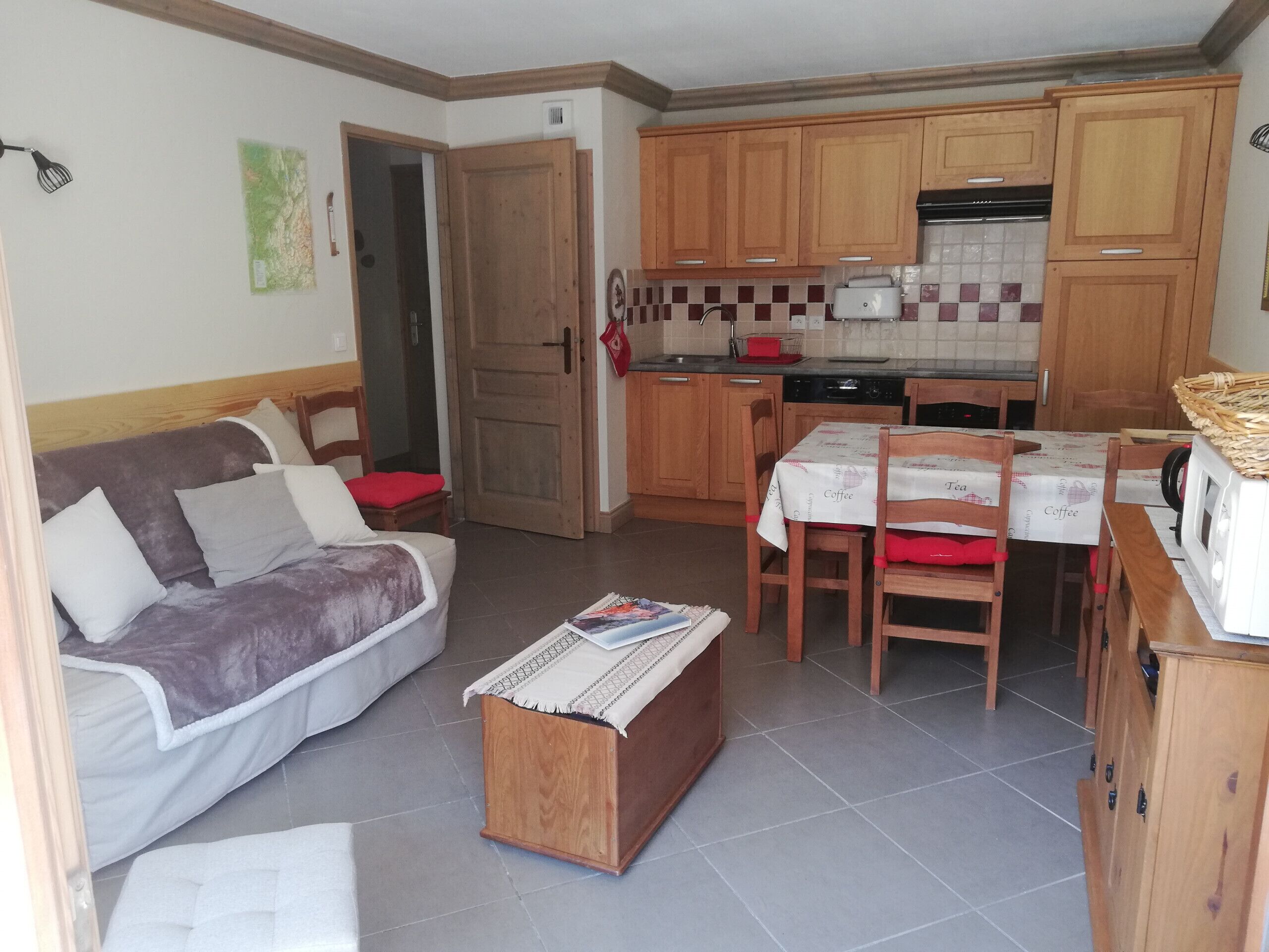 A compact living space with a sofa, a small wooden table, a kitchen area with wooden cabinets, and a dining table with chairs.