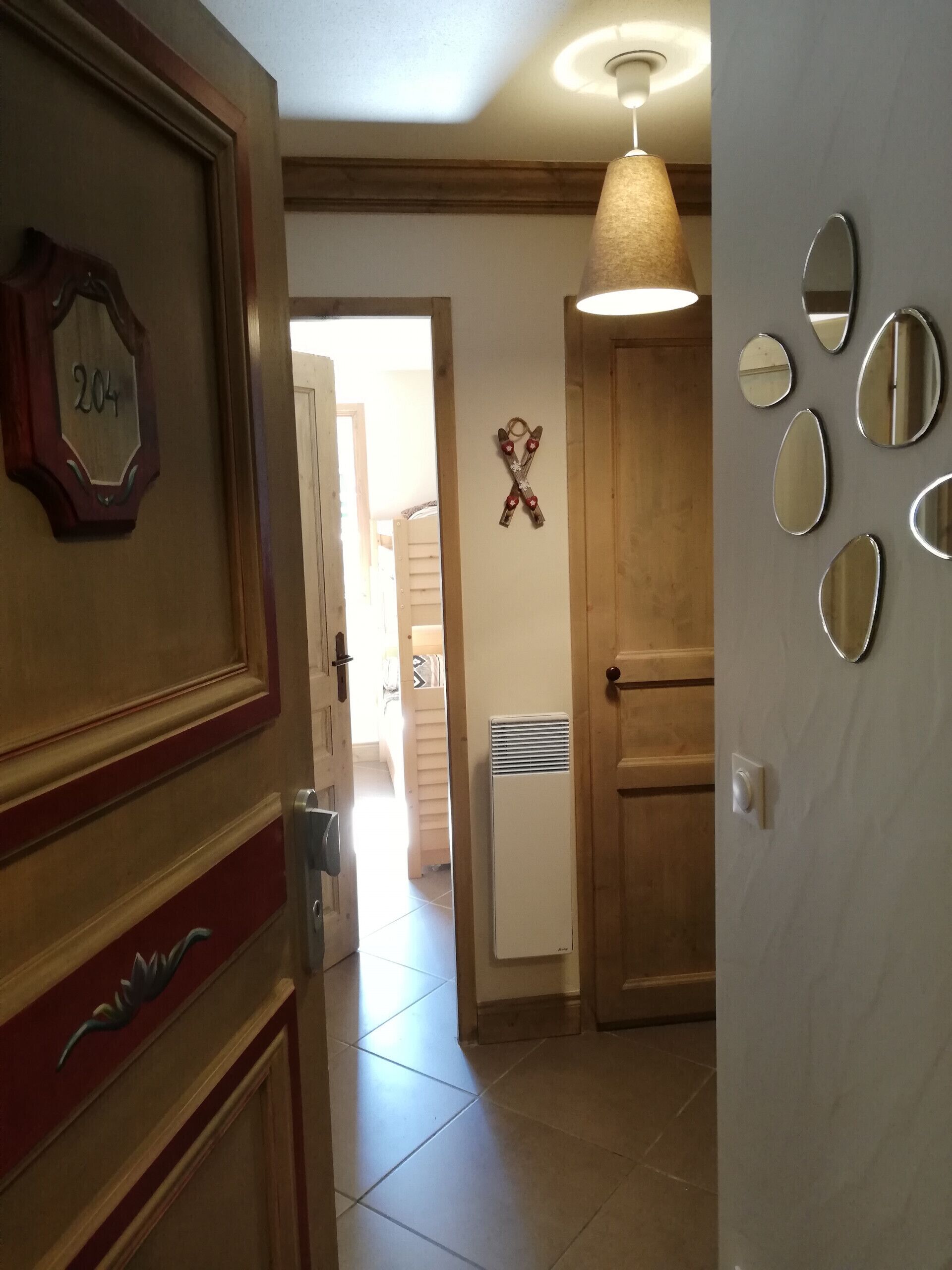 Un pasillo con una puerta de madera con el número '204', una lámpara colgante y un muro con varios espejos.