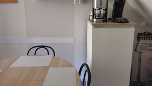 Una cocina compacta con cafetera, repisa con objetos varios y un armario blanco.