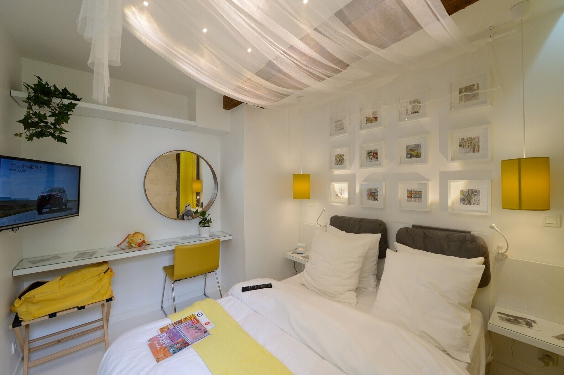 A hotel room with a bed, a desk with a chair, a mirror, a television, and wall-mounted lights.