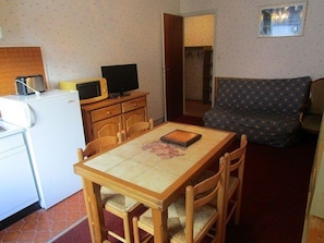 Un ambiente compatto con angolo cottura, un tavolo da pranzo con sedie, un divano e una televisione su un mobile in legno.