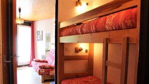 A room with bunk beds, a wooden ceiling, and a door leading to another room.