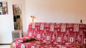 A cozy living room with a red patterned sofa, a wooden side table, and a radiator.