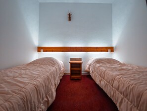 Een kamer met twee bedden, een houten hoofdbord, een klein houten nachtkastje en een wandlamp.