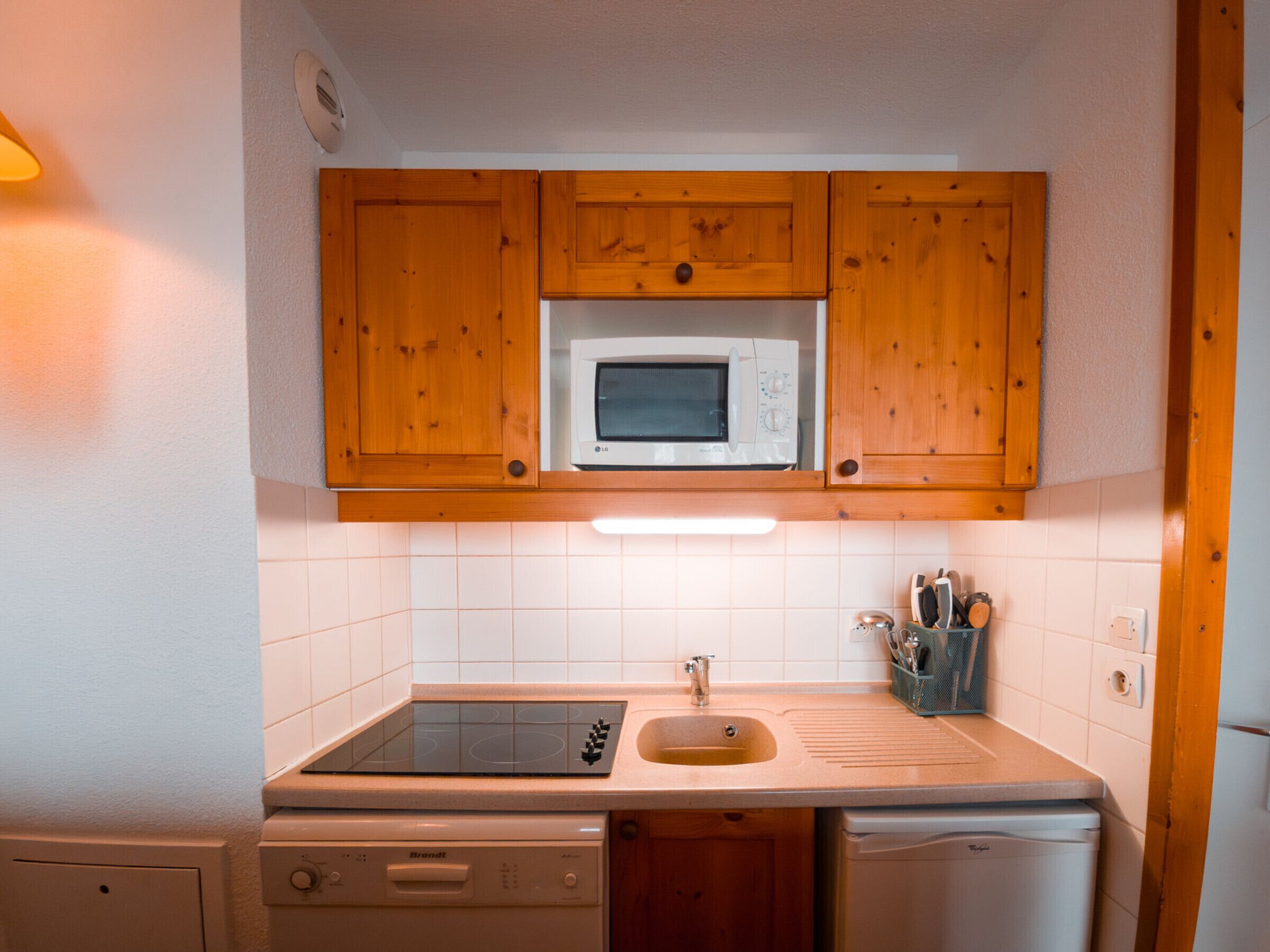 Una cocina compacta con armarios de madera, un microondas, un fregadero y un lavavajillas.