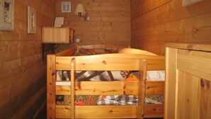 A wooden cabin room with a bunk bed, a small desk, and a wall-mounted lamp.