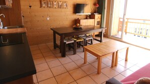 A wooden cabin interior with a kitchen area, a dining table, and a sofa.