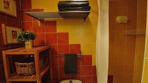 Un baño con pared de azulejos, repisa con toallas, inodoro y cortina de ducha.