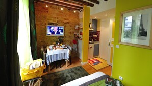 Una habitación acogedora con pared de piedra, televisor, zona de comedor con mesa y cama.