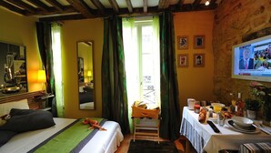 Habitación de hotel con cama, escritorio con productos para el desayuno, televisor y ventana grande con cortinas.