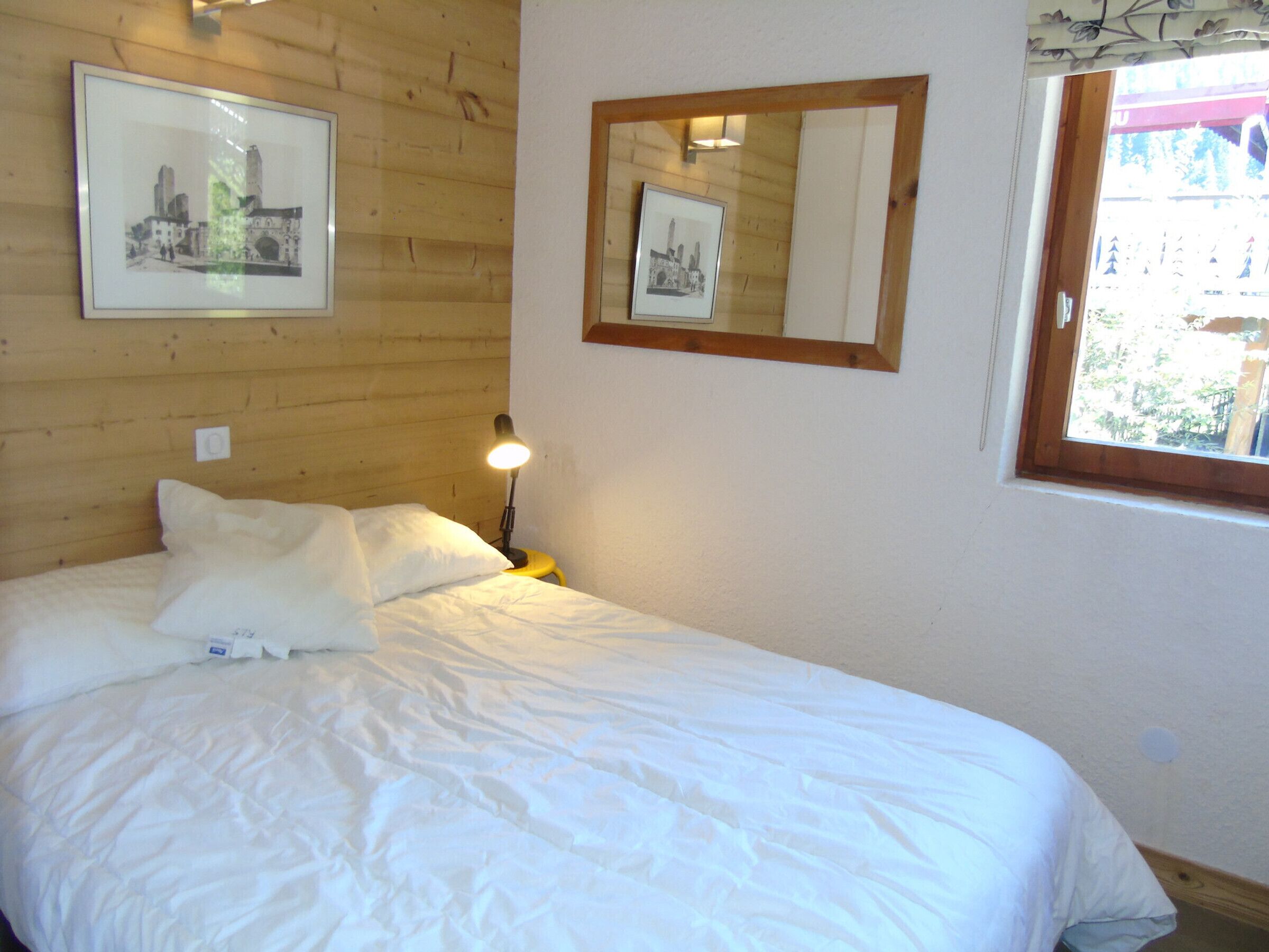 A bed with white bedding, a nightstand with a lamp, and two framed pictures on the wall.