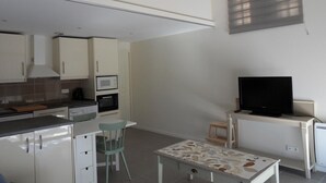 A compact kitchen with a microwave, stove, and cabinets. There's a small dining table with a chair, and a TV on a stand. - Gîte in a quiet house (Vidauban)