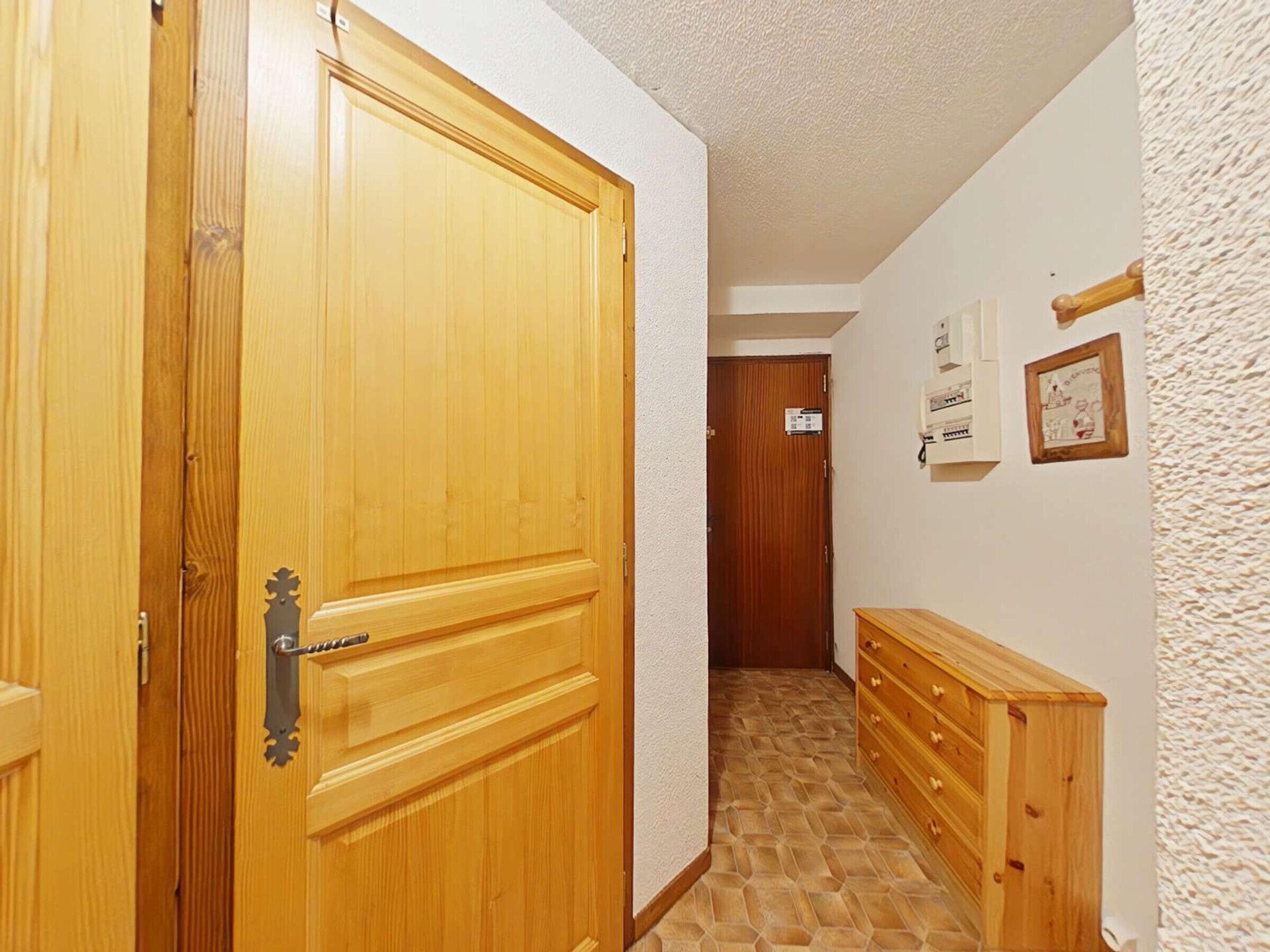 Käytävä, jossa on puinen ovi, puinen lipasto ja laatoitettu lattia.
