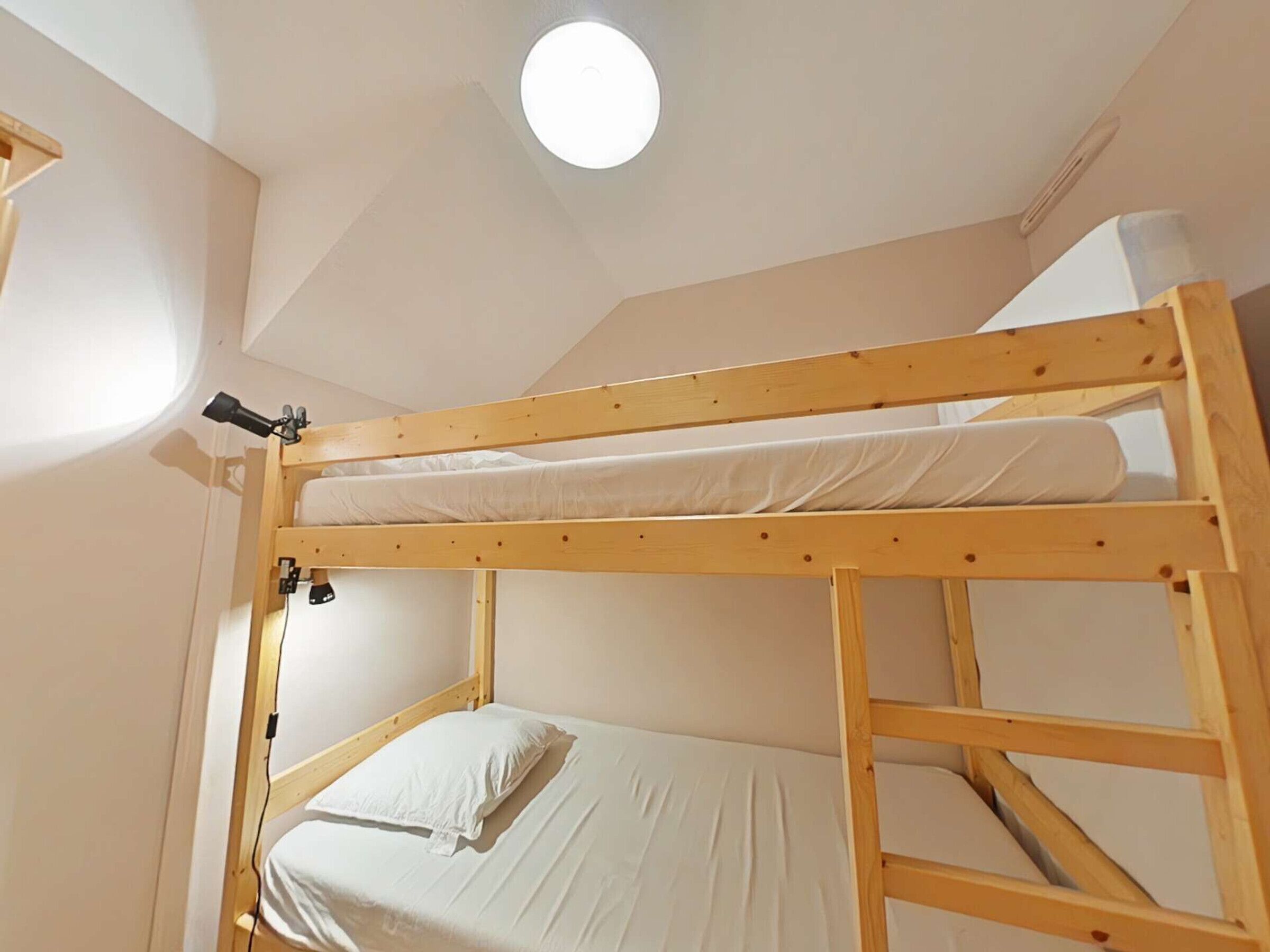 A bunk bed with a headboard, a single bed below, and a ceiling light.
