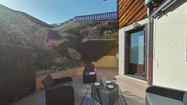 An outdoor patio with a checkered floor, a wicker sofa, and a table set with glasses.