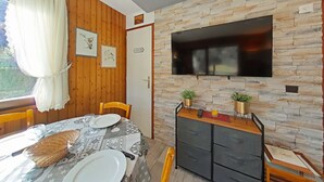A dining area with a table set for two, a TV mounted on a stone wall, and a door labeled "CUISINE".