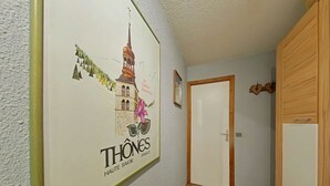 A hallway with a framed poster of Thônes, Haute Savoie, France, a wooden wardrobe, and a door.
