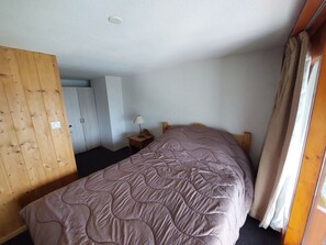 A bedroom with a bed, a wooden wardrobe, a nightstand with a lamp, and a window with curtains. - Charming duplex for 4 with stunning views in Arc 1800 (Les Arcs 1800)