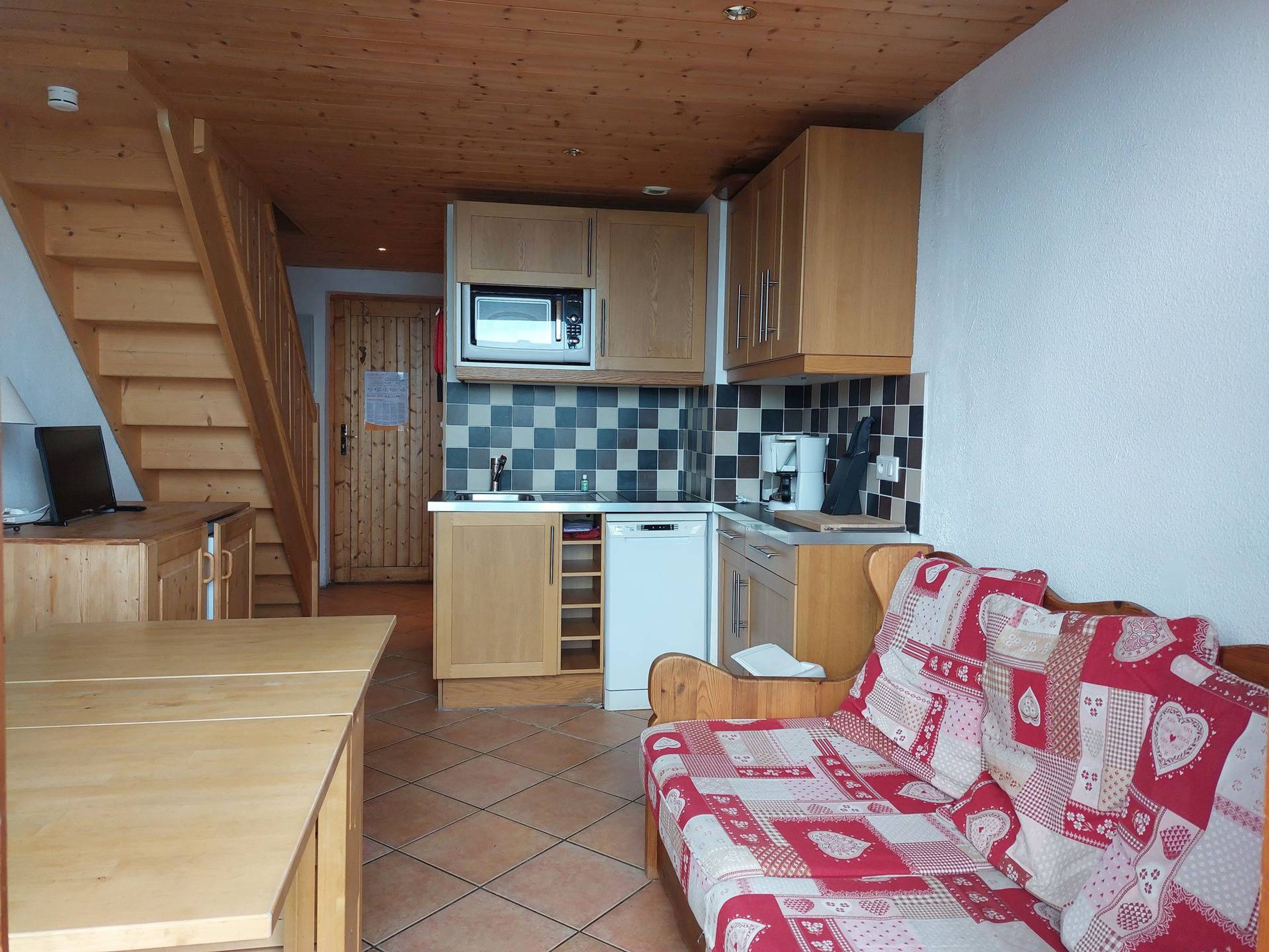 A compact kitchen with wooden cabinets, a microwave, and a small refrigerator.