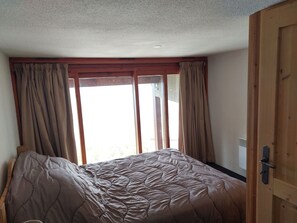 A bedroom with a bed, curtains, a wooden door, and a window.
