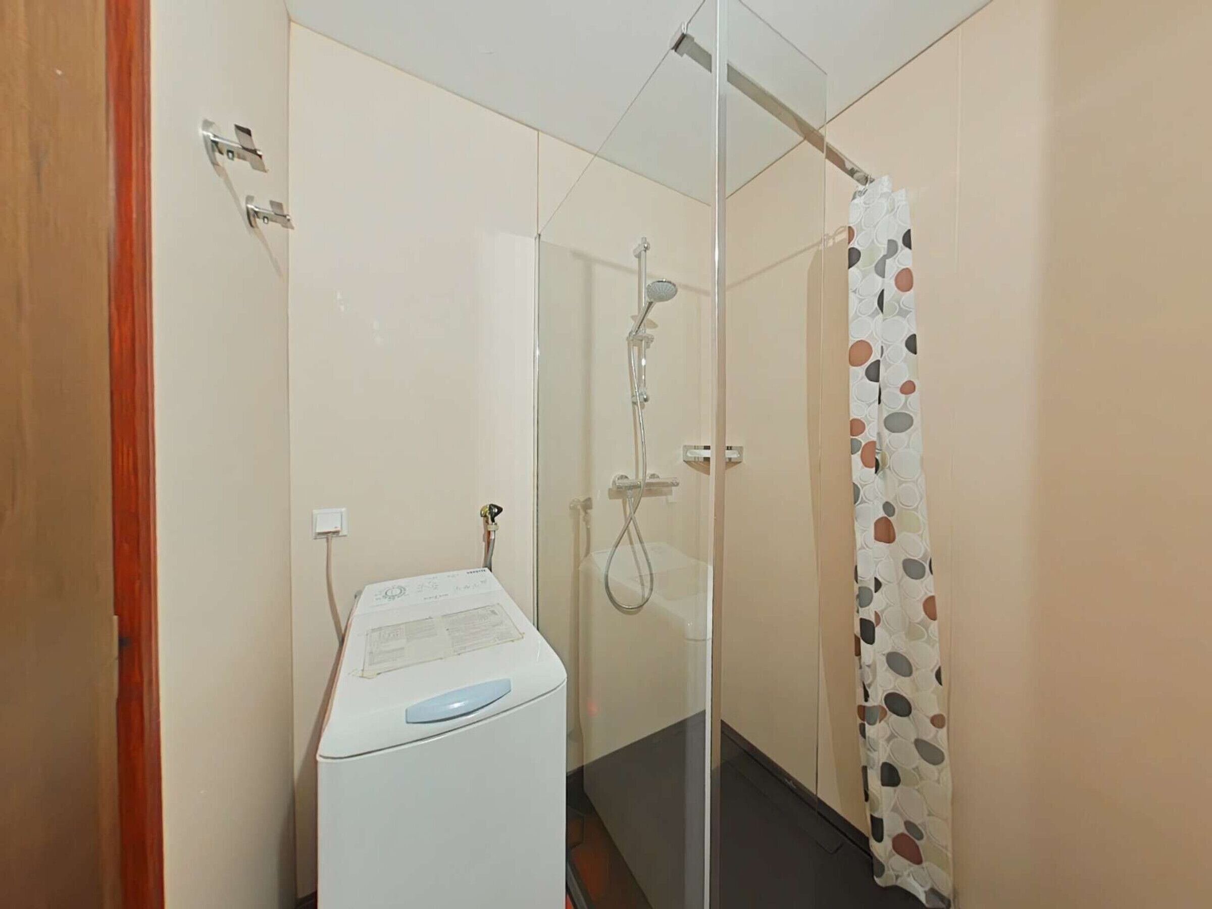 A compact bathroom with a glass shower enclosure, a white washing machine, and a patterned shower curtain.