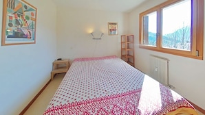 Ein Schlafzimmer mit einem Bett, einem Heizkörper, einem Fenster mit Blick und zwei an der Wand befestigten Regalen.