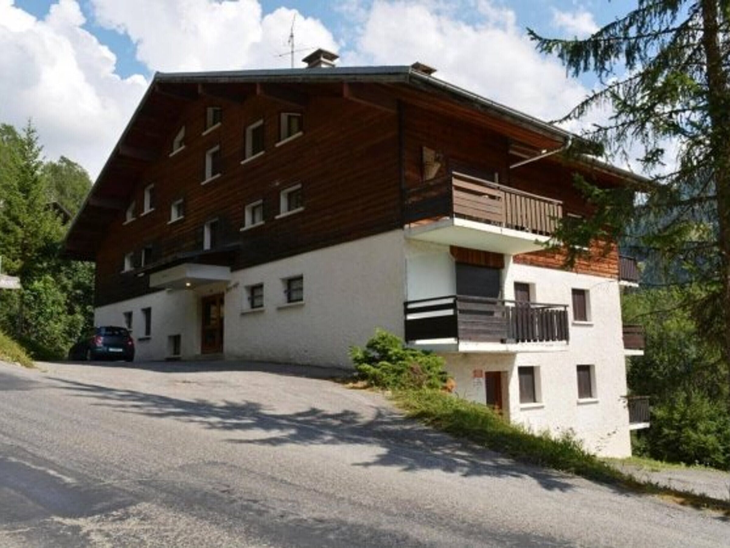 Un edificio a più piani con tetto spiovente e balconi, con un'auto parcheggiata di fronte.