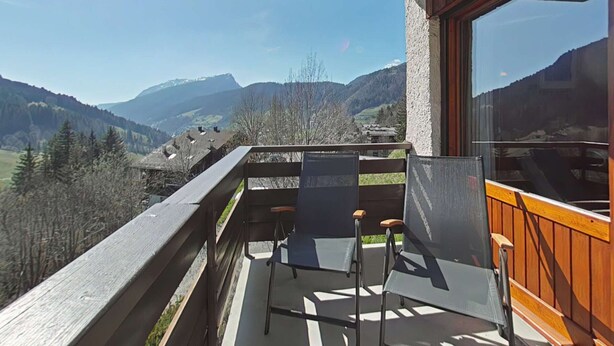 Ein Balkon mit zwei Stühlen und einem Tisch, mit Blick auf eine Berglandschaft.