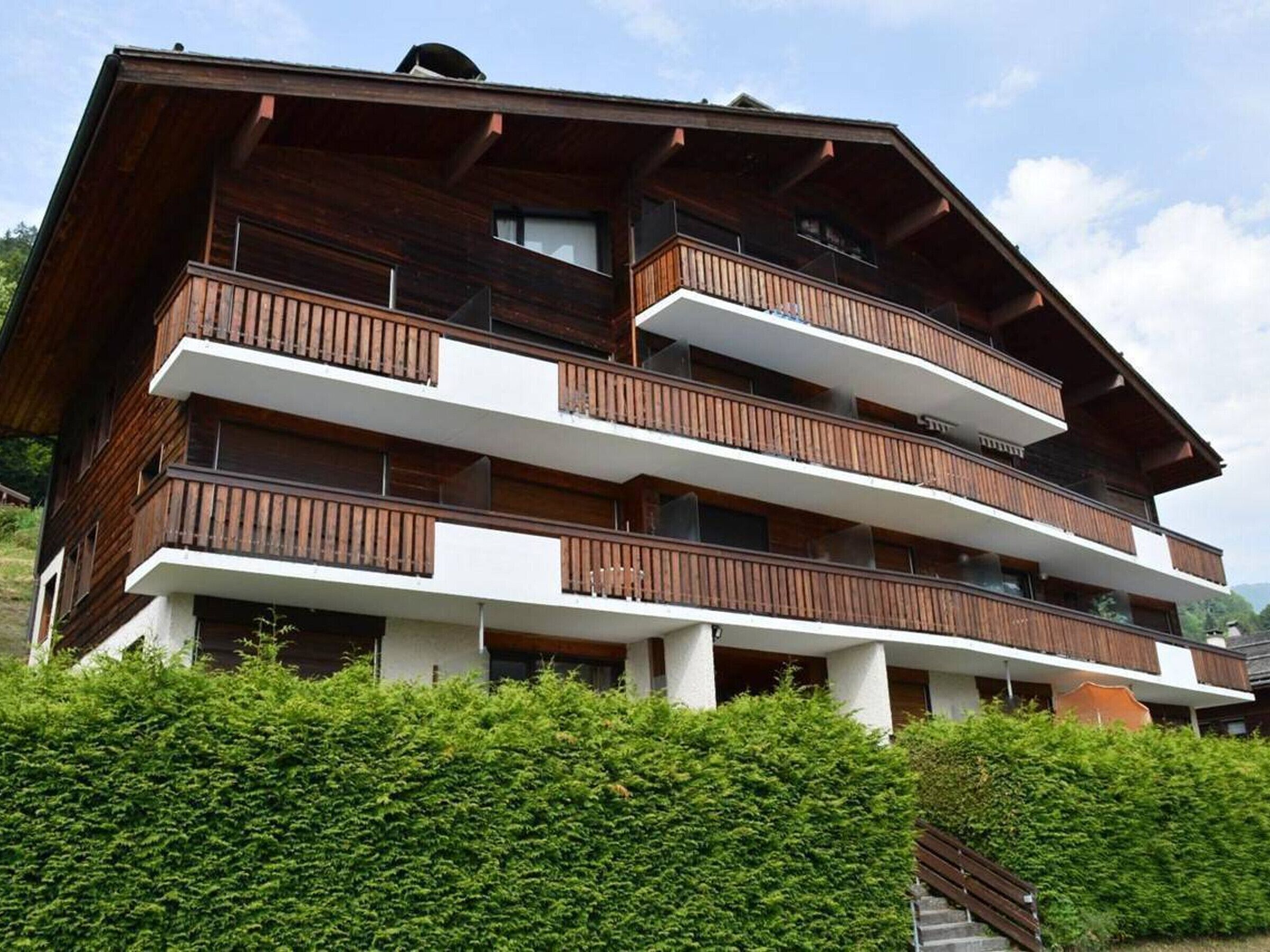 Un edificio de madera de varios pisos con balcones, rodeado de vegetación.