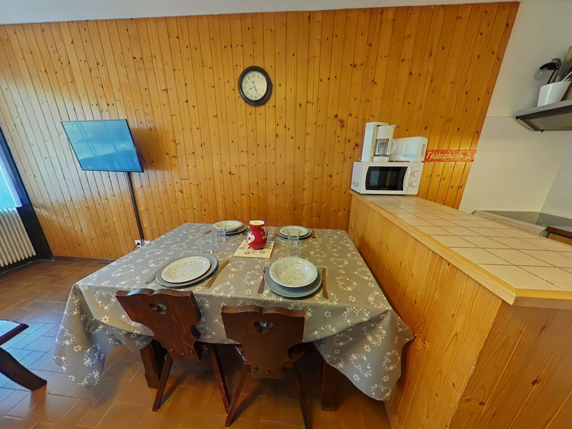 Un comedor con pared de madera, un reloj, un microondas y un televisor.