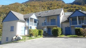 A row of two-story buildings with balconies, a parking lot in front, and a mountain in the background. - Cozy 3-Room Duplex with Balcony, Parking, Near Ski Lift, Sleeps 4 (Cauterets)