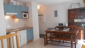 A compact kitchen with blue cabinets, a microwave, a stove, and a dishwasher. There is a dining table with chairs and a bench. - Cozy 3-Room Duplex with Balcony, Parking, Near Ski Lift, Sleeps 4 (Cauterets)