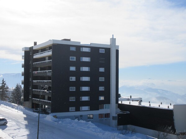 A multi-story building with a flat roof, several windows, and a parking area with a car.