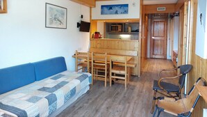 A cozy room with a blue sofa, wooden dining table, and chairs. A kitchen area is visible with a microwave and cabinets. - 2-room apartment 6 ppl, pets allowed, southwest balcony, close to slopes (Les Arcs 1800)