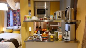 A compact hotel room with a kitchenette, a bed with colorful pillows, and a view of a colorful interior.