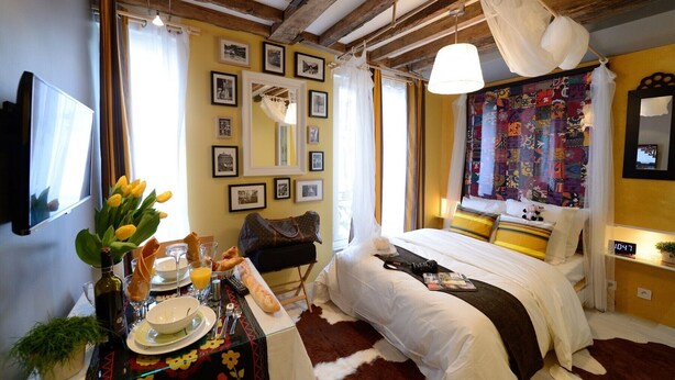 A cozy bedroom with a bed, a bedside table with a lamp, a mirror, and a colorful quilt.
