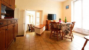 A kitchen with wooden cabinets, a dining table with chairs, a television, and a window.