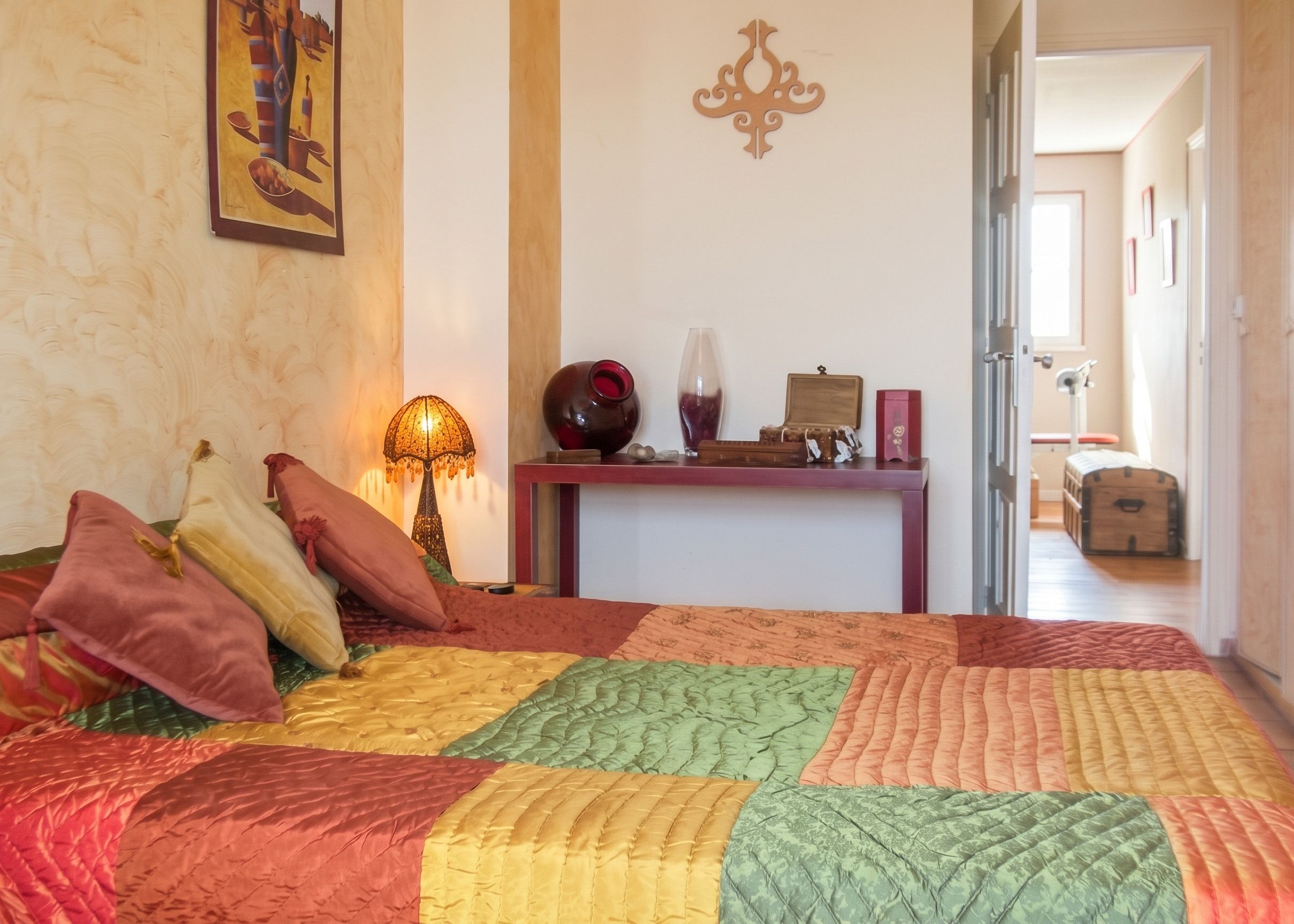 Ein Schlafzimmer mit einem Bett, Kissen, einem Nachttisch, einer Lampe und einer Wanddekoration.