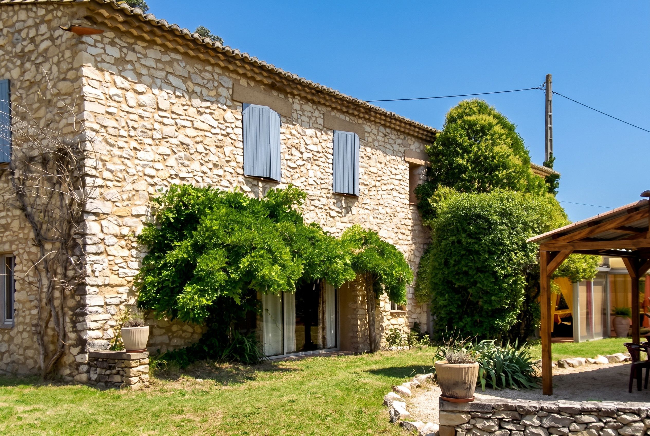 A stone building with a covered porch, a large tree, and a small garden area.