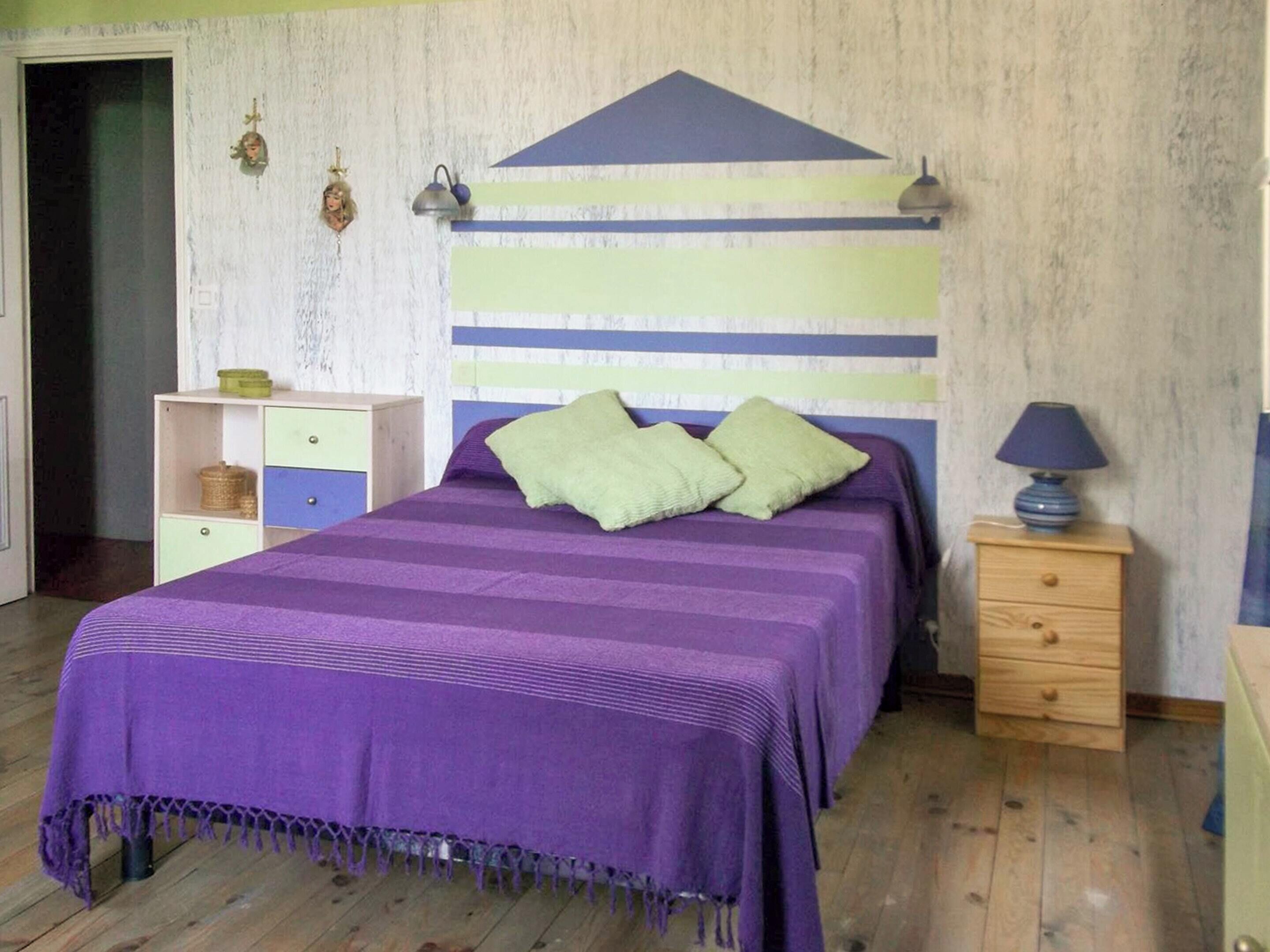 A bedroom with a bed, a nightstand, a dresser, and a wall with a striped pattern.