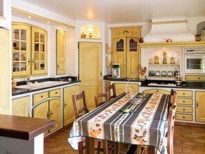 A kitchen with yellow cabinets, a dining table with a floral tablecloth, and a stove.